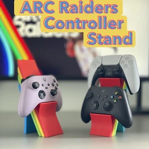 Pode incluir: Imagem de suportes de comando com o texto "ARC Raiders Controller Stand". Os suportes são vermelhos, amarelos, verdes e azuis. São exibidos três comandos de jogo: um comando Xbox lilás claro, um comando Xbox preto e um comando PlayStation branco.