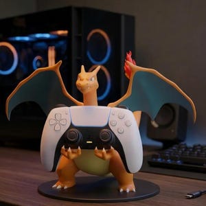 Puede incluir: Una figura naranja de Charizard de pie sobre una base circular negra, sosteniendo un mando de videojuego blanco y negro en sus garras. El personaje presenta alas de color verde azulado y una llama en la punta de la cola, en posici&oacute;n erguida.