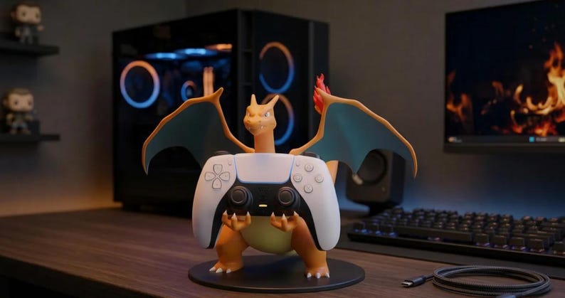 Puede incluir: Una figura naranja de Charizard de pie sobre una base circular negra, sosteniendo un mando de videojuego blanco y negro en sus garras. El personaje presenta alas de color verde azulado y una llama en la punta de la cola, en posici&oacute;n erguida.