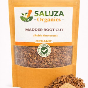 Könnte beinhalten: Eine Packung Madder Root Cut (Rubia tinctorum) von Saluza Organics. Der braune Inhalt ist durch ein klares Fenster sichtbar. Ein kleiner Haufen der Wurzel und des Pulvers befindet sich vor der Packung. Die Packung hat ein grünes und orangefarbenes Logo und das Wort "Organic".
