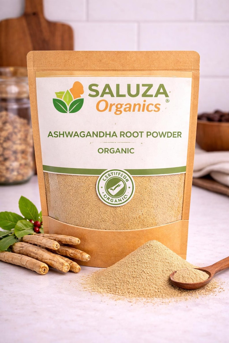 Puede incluir: Bolsa de papel marr&oacute;n con polvo de ra&iacute;z de ashwagandha org&aacute;nico, con la marca "SALUZA Organics". Un peque&ntilde;o mont&oacute;n de polvo y una cuchara de madera est&aacute;n frente a la bolsa. Tambi&eacute;n se ven varias ra&iacute;ces de ashwagandha.