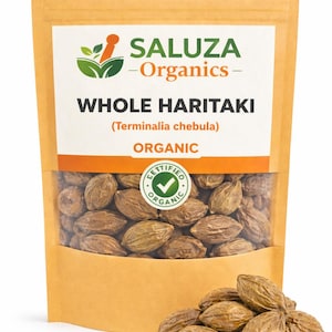 以下が含まれることがあります： 全ハリティキの種子が入った透明窓付きの茶色の紙袋。袋には「SALUZA - Organics」と「WHOLE HARITAKI (Terminalia chebula) ORGANIC」の文字。袋の前にはハリティキの種子の小さな山がある。