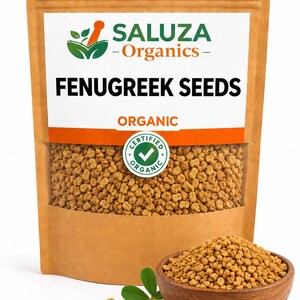 Pode incluir: Um saco de papel castanho com sementes de feno-grego orgânicas, uma etiqueta branca com a inscrição SALUZA Organics FENUGREEK SEEDS e um selo orgânico certificado verde. Uma taça de madeira com sementes está à frente com um pequeno ramo verde.