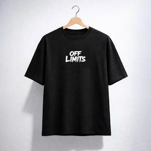 May include: Black t-shirt with the white text "OFF LIMITS" across the chest. The shirt is hanging on a wooden hanger against a white background. The text has a bold, slightly distressed font.