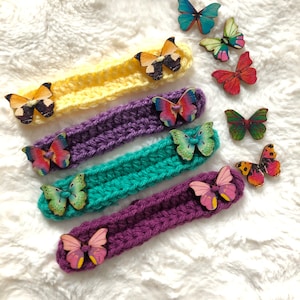 May include: Four crocheted headbands with colorful butterfly embellishments. The headbands are in yellow, purple, green, and purple. The butterflies are made of wood and have different colors and patterns.