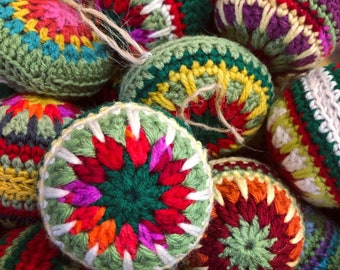 Puede incluir: Una colección de adornos esféricos con intrincados patrones de ganchillo en colores vibrantes que incluyen rojo, verde, amarillo, morado y naranja. Cada adorno está elaborado con puntadas de hilo detalladas e incluye un lazo de yute para colgar.
