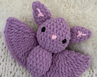Pode incluir: Um morcego de pelúcia feito à mão em crochê com fio roxo grosso. O morcego apresenta duas asas grandes, orelhas pontudas com detalhes costurados em rosa claro, um pequeno nariz rosa claro e dois olhos de segurança pretos e redondos.