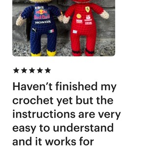 May include: Two handmade crochet dolls representing race car drivers. The left doll wears a yellow helmet and a dark blue racing suit with Red Bull and Honda logos. The right doll wears a red helmet and a red racing suit with Ferrari branding.