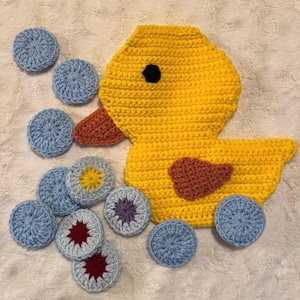 May include: A yellow crocheted duck with brown and orange accents, surrounded by blue crocheted circles.