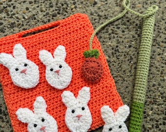 May include: A bright orange square crochet mat featuring five white bunny head appliques with black eyes and pink noses, accompanied by a small brown crochet carrot attached to a long green crochet stem with a thin green cord.