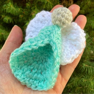 Op de afbeelding: Een gehaakt engel ornament met een wit lichaam, turquoise vleugels en een grijs hoofd.