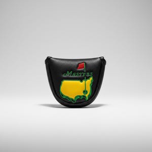 Könnte beinhalten: Schwarze Golf-Putter-Abdeckung aus Leder mit dem Masters Tournament-Logo. Die Abdeckung hat eine strukturierte Oberfläche und ein Design einer gelben Karte mit einer grünen Flagge und dem Wort "Masters" in Grün.