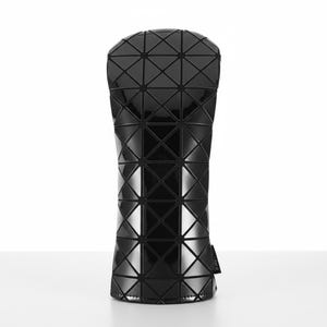 May include: A black golf club head cover with a geometric, triangular pattern. The cover has a glossy finish and is likely made from a durable material. The design is modern and sleek, suitable for protecting golf clubs.