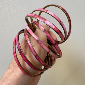 Puede incluir: Conjunto de seis pulseras de oro y rosa con un diseño de mosaico. Las pulseras están apiladas unas sobre otras.