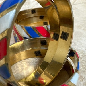 Puede incluir: Conjunto de cuatro pulseras de oro con rayas de esmalte rojo, blanco y azul. Cada pulsera tiene las palabras "Made in India" estampadas en el interior.