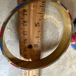 Puede incluir: Un brazalete de lat&oacute;n con un patr&oacute;n geom&eacute;trico rojo, blanco y azul. El brazalete tiene un di&aacute;metro de aproximadamente 5 cm.