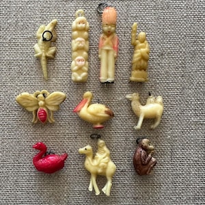 May include: A selection of small, vintage ornaments in various shapes, including a lizard, a stack of monkeys, a soldier, a figure with an upraised arm, a butterfly, a pelican, a camel, a swan, a figure on a camel, and a monkey.