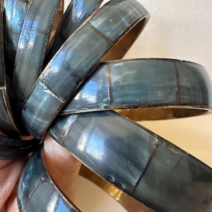 Puede incluir: Un conjunto de ocho brazaletes de color azul oscuro y dorado con un patrón de azulejos. Los brazaletes están hechos en la India.