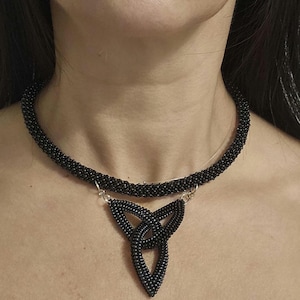 May include: A black beaded choker necklace featuring a central triangular pendant made of interconnected beaded loops. The necklace is constructed from small, uniform black beads and is attached to the pendant with silver-toned metal jump rings.