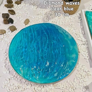 Könnte beinhalten: Runde, klare blaue Kunst aus Kunstharz mit Wellenmuster. Das Kunstwerk hat einen Durchmesser von 30 cm und trägt den Text "Diamond waves clear blue". Weiße Kieselsteine umgeben das Kunstwerk.