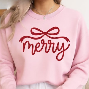 Könnte beinhalten: Hellrosa Sweatshirt mit dem Wort "merry" in roter Schrift, gekrönt von einem roten Schleifendesign. Das langärmlige Oberteil ist ein festliches Kleidungsstück für die Feiertage.