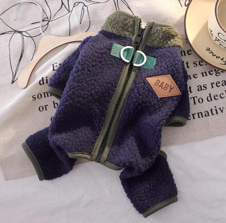 May include: A navy blue dog jacket with a green collar and trim. The jacket has a zipper closure and a small brown patch that says "BABY". The jacket is made of a soft, fuzzy material.