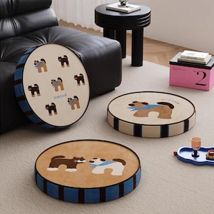 Könnte beinhalten: Runde beige Kissen mit Hunde- und Katzenillustrationen. Die Kissen haben einen blau-braun gestreiften Rand. Auf einem Kissen steht das Wort "Bonjour".