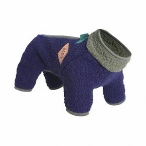 May include: A navy blue dog coat with a gray collar and trim. The coat has a soft, textured appearance and features a small pink label with the word "BABY" on it. The coat is designed to cover the dog's body and legs.