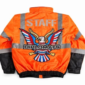 May include: Vibrant orange bomber jacket with black sleeves and reflective stripes. The back displays the word "STAFF" in silver and an eagle emblem with red, white, and blue wings, and the word "DIPLOMATS".