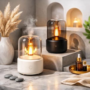 Peut inclure: Deux diffuseurs d'aromathérapie, un blanc et un noir, avec un dôme en verre et une lumière chaude. Le diffuseur blanc est à gauche et le noir à droite. Les deux sont sur une surface grise. Un vase avec des plantes séchées est à gauche.