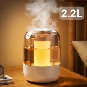 Könnte beinhalten: Weißer und klarer Luftbefeuchter mit 2,2L Fassungsvermögen. Zylindrisches Design mit weißer Basis und transparentem Oberteil. Dampf steigt auf, das Innere leuchtet warm. Steht auf einer Holzoberfläche.