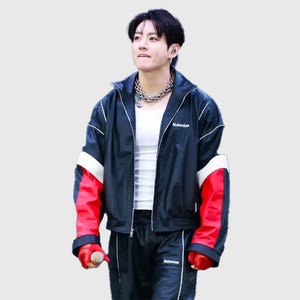 May include: A black zip-up jacket with white piping and red panels on the sleeves, worn over a white tank top. The jacket features the brand name Nahmias in white text on the chest. The outfit includes matching black track pants with white piping.