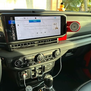 Puede incluir: Interior del salpicadero de un coche con una gran pantalla de informaci&oacute;n que muestra informaci&oacute;n musical. La pantalla muestra la canci&oacute;n "Twelve Days of Christmas". Un peque&ntilde;o patito de goma est&aacute; sentado en el salpicadero.