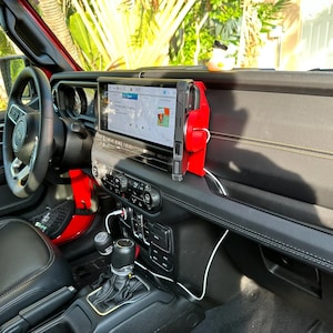 Puede incluir: Vista interior de un Jeep Wrangler rojo. El salpicadero cuenta con una gran pantalla de infoentretenimiento, un soporte rojo para el tel&eacute;fono y varios controles. Un patito de goma est&aacute; en el salpicadero. El volante y los asientos son negros.