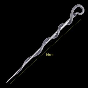 Puede incluir: Una horquilla plateada con un diseño de serpiente enroscada que se envuelve a lo largo del pasador. La cabeza de la serpiente forma un bucle en la parte superior. Una línea discontinua amarilla indica una longitud de 16 cm en el accesorio.