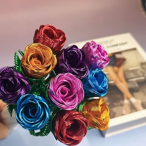 May include: A vibrant bouquet of wire roses in various colours, including red, orange, purple, pink, and blue. The roses are made with detailed wire work, with green wire stems and leaves. The flowers are arranged in a bouquet, suitable for gifting or home decoration.