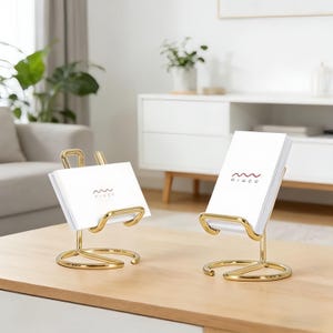 May include: Two gold-toned metal stands with a circular base and a curved support arm, each holding a stack of white rectangular cards. The cards feature a small red wavy line graphic above the text "MIWOO" printed in a dark red font.