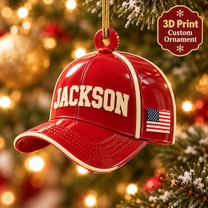 May include: A red baseball cap ornament with a cream-colored brim edge and the name JACKSON in cream lettering across the front. A small American flag patch is on the side. The ornament hangs from a gold cord and features 3D Print Custom Ornament text.