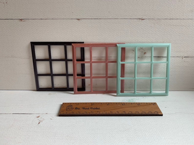 Pu&ograve; includere: Tre cornici per finestre quadrate in nero, rosa antico e verde menta, ciascuna con un design a griglia di nove riquadri. Un righello di legno &egrave; posizionato davanti, mostrando che le cornici misurano circa 9 cm in larghezza e altezza.