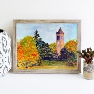 K&ouml;nnte beinhalten: Aquarellmalerei eines hohen Ziegelturms mit einem Zifferblatt, umgeben von B&auml;umen mit Herbstlaub. Der Turm steht vor einem blauen Himmel mit wei&szlig;en Wolken.