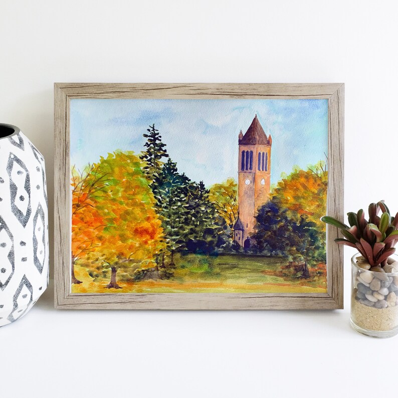 K&ouml;nnte beinhalten: Aquarellmalerei eines hohen Ziegelturms mit einem Zifferblatt, umgeben von B&auml;umen mit Herbstlaub. Der Turm steht vor einem blauen Himmel mit wei&szlig;en Wolken.