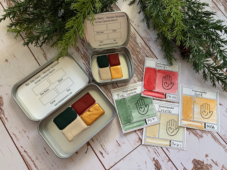 Puede incluir: Un juego de seis acuarelas en una lata de metal. Los colores son verde pino, baya, crema, oro y dos tonos de verde. La lata tiene una etiqueta que dice "The Hare Painter - Acuarela hecha a mano Paleta de Navidad festiva".