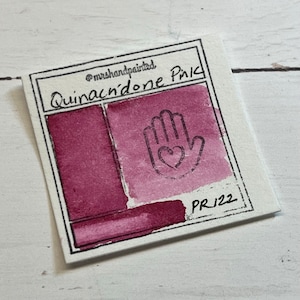 Peut inclure: Une carte d'échantillon de peinture aquarelle avec le texte "Quinacridone Pink" et "PR122". La carte montre un échantillon de couleur rose avec une icône d'empreinte de main.