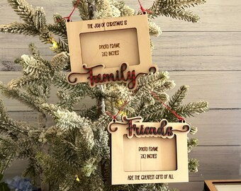May include: Two wooden Christmas ornaments with photo frames. The top ornament says "The joy of Christmas is Family" and the bottom ornament says "Friends are the greatest gifts of all". Both ornaments have a 3x2 inch photo frame.