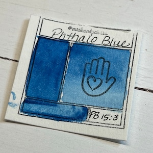 May include: A watercolor paint swatch card showing the color Phthalo Blue. The card has a handprint with a heart in the center and the text "PB 15:3" in the bottom right corner.