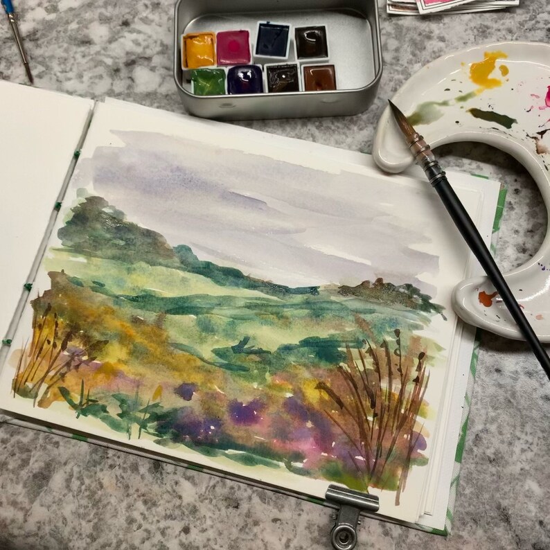May include: A watercolor painting of a landscape with rolling hills, green fields, and a cloudy sky. The painting is done in shades of green, brown, and purple.