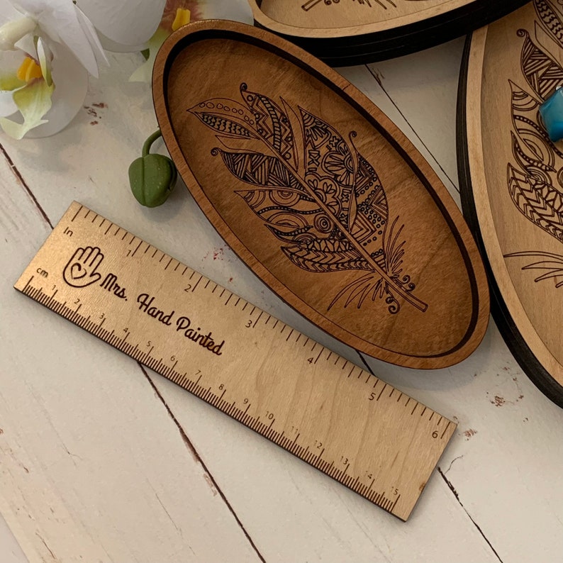 May include: Wooden oval tray with a detailed feather design. The feather is etched into the wood and filled with intricate patterns. A wooden ruler with inch measurements and the text "Mrs. Hand Painted" is in the foreground. The tray is approximately 6 inches long.