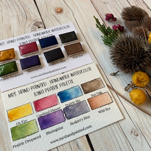 May include: Two cards showing a watercolor paint palette with the title "Mrs. Hand Painted - Handmade Watercolor Iowa Prairie Palette". The palette includes colors like "Prairie Dropseed", "Blazingstar", "Reakirt's Blue", "Wild Rye", "Ox Eye", "Cardinal Flower", "Prairie Sky", "Bur Oak".