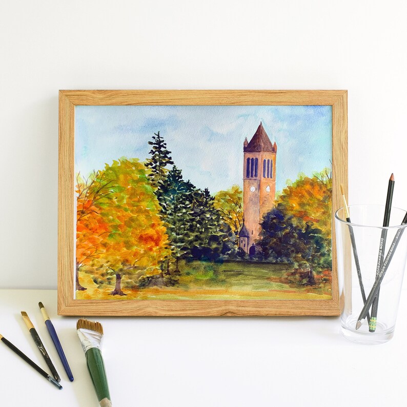 K&ouml;nnte beinhalten: Aquarellmalerei eines Ziegelturms mit einer Uhr, umgeben von B&auml;umen mit Herbstlaub. Der Turm steht vor einem blauen Himmel mit wei&szlig;en Wolken.