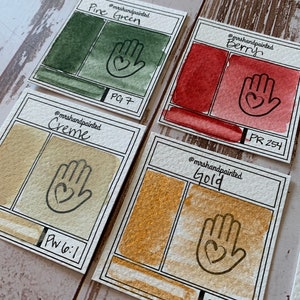 Puede incluir: Cuatro muestras de pintura acuarela con muestras de color pintadas a mano y los n&uacute;meros de pigmento correspondientes. Los colores son Verde pino (PG7), Crema (PW6:1), Baya (PR 254) y Oro.